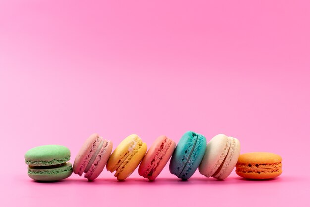 Een vooraanzicht Franse macarons om heerlijk kleurrijk geïsoleerd op roze, cakekoekje banketbakkerij