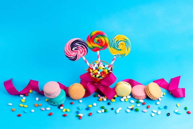 Een vooraanzicht franse macarons samen met snoepjes en lollies kleurrijke snoepjes allemaal op blauw