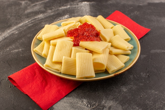 Een vooraanzicht gekookte Italiaanse deegwaren met tomatensaus binnen plaat op de grijze Italiaanse het voedselmaaltijd van lijstdeegwaren