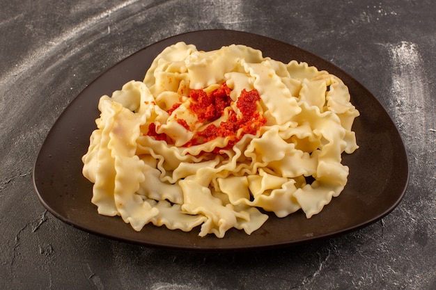 Een vooraanzicht gekookte Italiaanse pasta met tomatensaus in plaat op het grijze oppervlak
