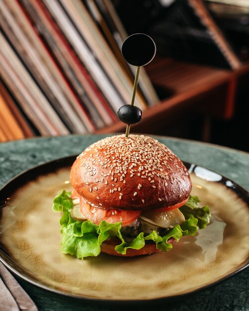 Een vooraanzicht hamburger lekker met groene salade en andere ingrediënten in ronde plaat op het donkere oppervlak