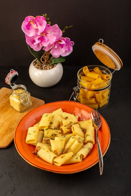 Een vooraanzicht italiaanse pasta gekookt lekker gezouten binnen ronde oranje plaat met bloemen binnen dip op ontworpen tapijt en donker bureau