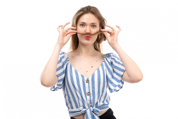 Een vooraanzicht jong aantrekkelijk meisje in gestreept blauw-wit t-shirt die zwarte jeans dragen die met haar haar in haar hand op het wit stellen