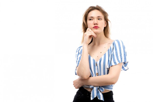 Een vooraanzicht jong aantrekkelijk meisje in gestreepte blauw-witte t-shirt die zwarte jeans dragen die denkend op het wit stellen