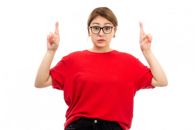 Een vooraanzicht jong aantrekkelijk meisje in rode t-shirt die zwarte jeans in zonnebril dragen die op het wit stellen