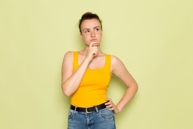 Een vooraanzicht jong wijfje in geel overhemd en jeans met denkende uitdrukking