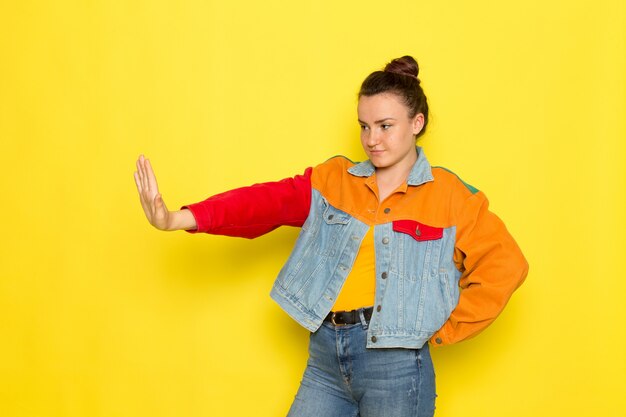 Een vooraanzicht jong wijfje in geel overhemd kleurrijk jasje en jeans het stellen