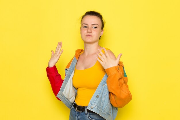 Een vooraanzicht jong wijfje in geel overhemd kleurrijk jasje en jeans het stellen