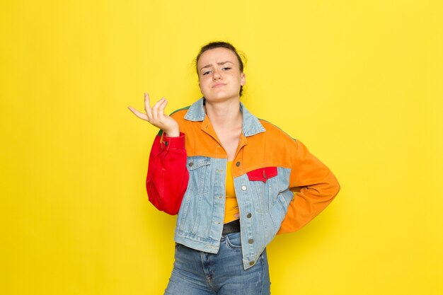 Een vooraanzicht jong wijfje in geel overhemd kleurrijk jasje en jeans het stellen