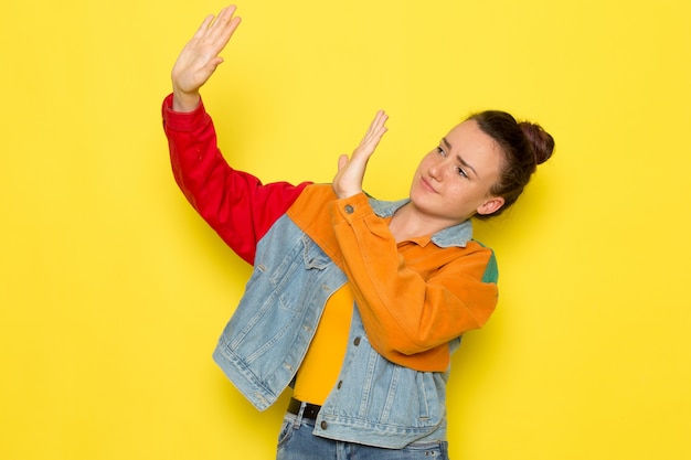 Een vooraanzicht jong wijfje in geel overhemd kleurrijk jasje en jeans het stellen