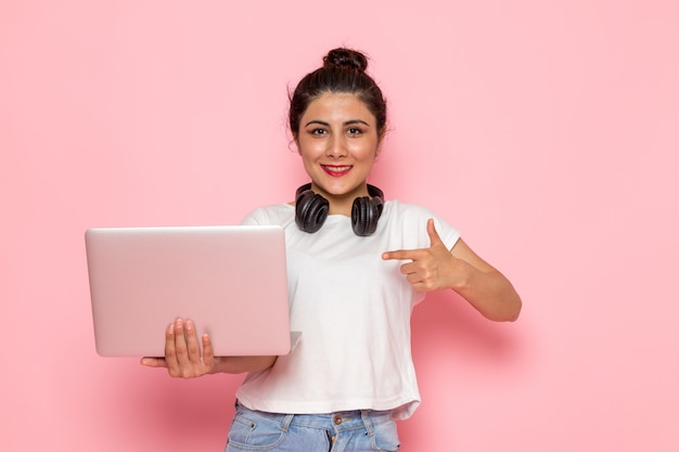 Een vooraanzicht jong wijfje in wit t-shirt en jeans die laptop met glimlach houden