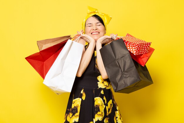 Een vooraanzicht jonge aantrekkelijke dame in geel-zwart bloem ontworpen jurk met geel verband op het hoofd poseren met shopping pakketten op de gele