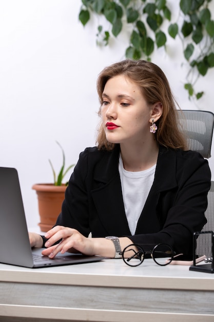 Een vooraanzicht jonge aantrekkelijke dame in zwarte jas en wit overhemd voor tafel werken met laptop werk zakelijke technologieën