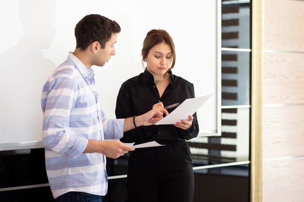 Gratis foto een vooraanzicht jonge aantrekkelijke zakenvrouw in zwart shirt, samen met jonge man bespreken van afbeeldingen op het bureau, terwijl de jonge dame haar werk leest document presentatie presentatie