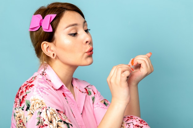 Een vooraanzicht jonge dame in bloem ontworpen roze jurk werkt met haar nagels op blauw