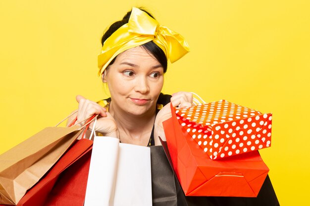 Een vooraanzicht jonge dame in geel-zwart bloem ontworpen jurk met geel verband op het hoofd poseren met shopping pakketten op de gele