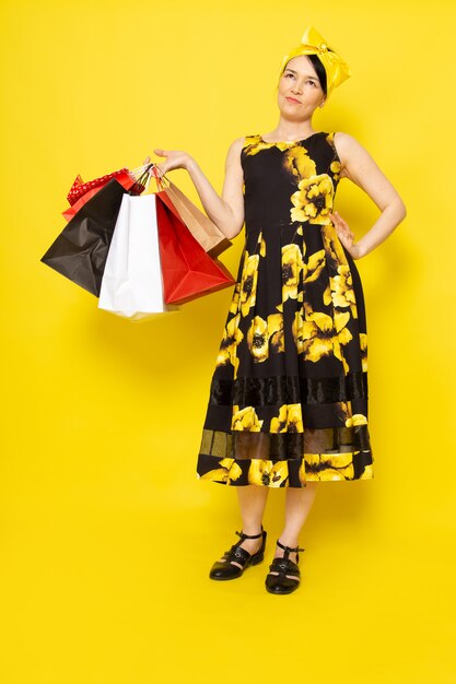 Een vooraanzicht jonge dame in geel-zwart bloem ontworpen jurk met gele bandage op het hoofd met boodschappenpakketten op de gele