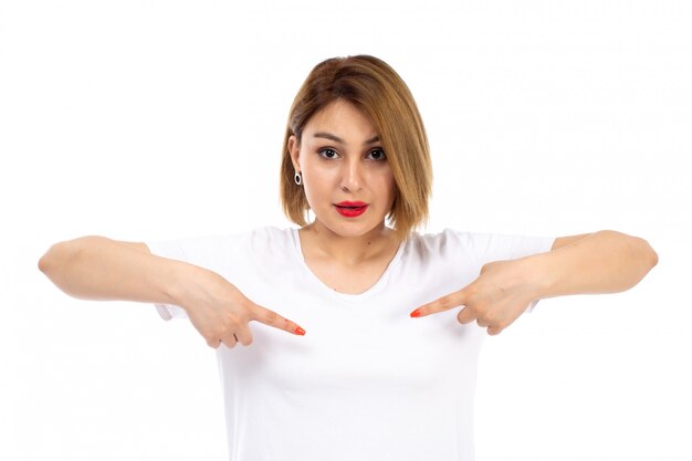 Een vooraanzicht jonge dame in het witte t-shirt stellen die haar vingers op het wit richten