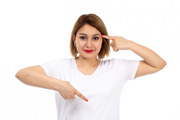 Een vooraanzicht jonge dame in het witte t-shirt stellen die op het wit glimlachen