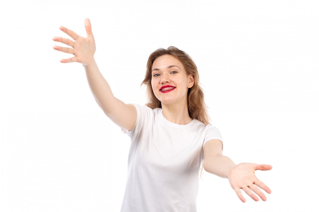 Een vooraanzicht jonge dame in het witte t-shirt stellen glimlachen gelukkig op het wit