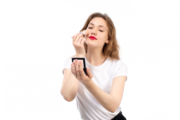 Een vooraanzicht jonge dame in wit overhemd en zwarte broek doen make-up op de witte