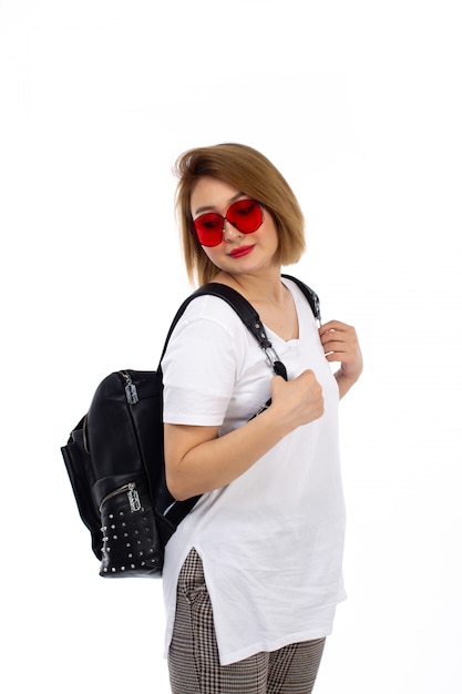 Een vooraanzicht jonge dame in witte t-shirt rode zonnebril zwarte tas lachend op de witte