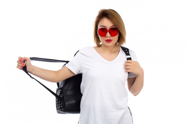 Een vooraanzicht jonge dame in witte t-shirt rode zonnebril zwarte tas op de witte