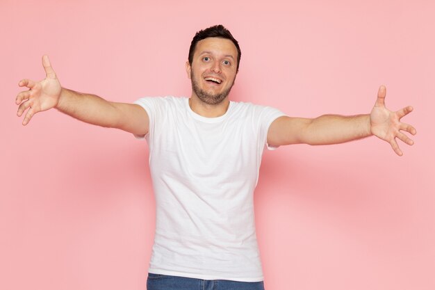 Een vooraanzicht jonge man in wit t-shirt en spijkerbroek met opgetogen uitdrukking op het roze bureau man kleur emotie pose