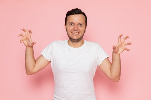 Een vooraanzicht jonge man in wit t-shirt en spijkerbroek poseren met grappige uitdrukking op het roze bureau man kleur emotie pose