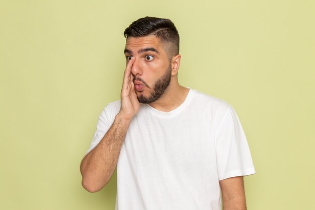 Een vooraanzicht jonge man in wit t-shirt fluisteren