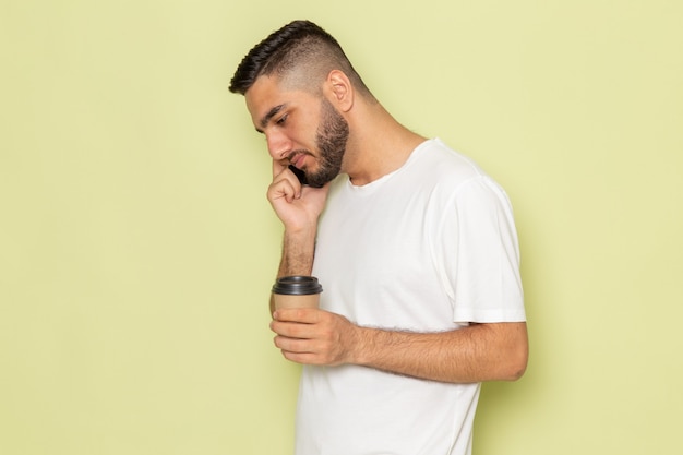 Een vooraanzicht jonge man in wit t-shirt koffiekopje te houden en te praten aan de telefoon