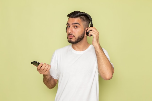 Een vooraanzicht jonge man in wit t-shirt met telefoon en luisteren naar muziek