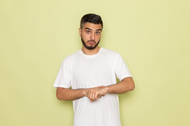 Een vooraanzicht jonge man in wit t-shirt wijzend op zijn pols
