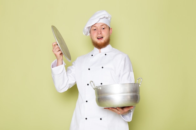 Een vooraanzicht jonge mannelijke kok in wit kokkostuum wit hoofd GLB die zilveren steelpan opgewekt houden