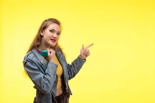 Een vooraanzicht jonge moderne vrouw in gele overhemd zwarte broek en de jas van Jean met het gekleurde oortelefoons stellen gelukkig glimlachen