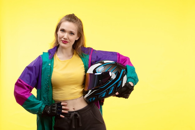 Een vooraanzicht jonge moderne vrouw in gele overhemd zwarte broek en het kleurrijke jasje houden van motocycle helm het stellen