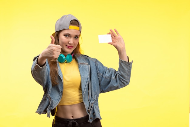 Een vooraanzicht jonge moderne vrouw in gele overhemd zwarte broek en jean jas met gekleurde koptelefoon