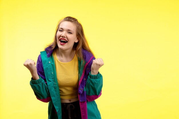 Een vooraanzicht jonge moderne vrouw in gele overhemd zwarte broek en kleurrijk jasje die gelukkige uitdrukking stellen