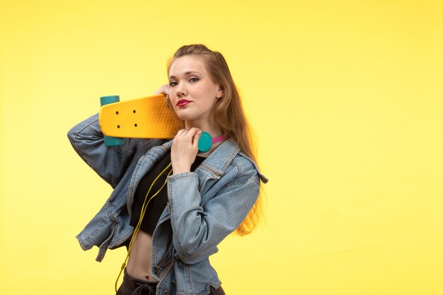 Een vooraanzicht jonge moderne vrouw in zwarte overhemd zwarte broek en jean jas met skateboard met gekleurde koptelefoon