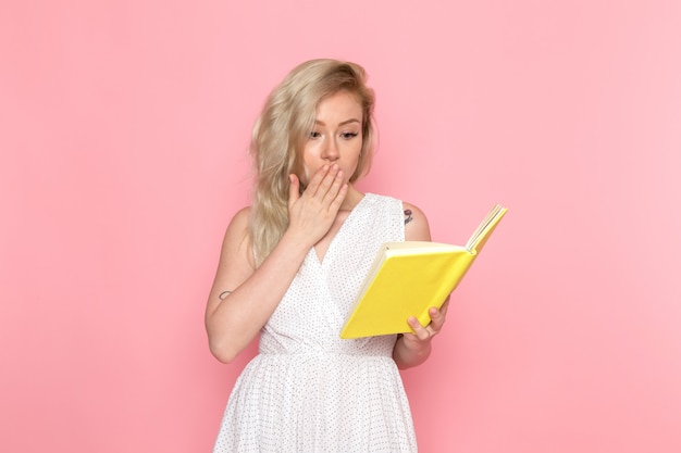 Een vooraanzicht jonge mooie dame die in witte kleding geel voorbeeldenboek houdt