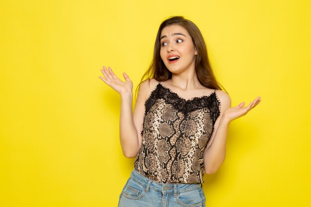 Een vooraanzicht jonge mooie dame in bruine blouse en spijkerbroek poseren