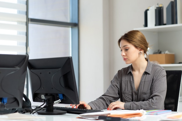 Een vooraanzicht jonge mooie dame in grijs shirt werken met de documenten met behulp van haar pc zit in haar kantoor tijdens het bouwen van overdag baanactiviteit