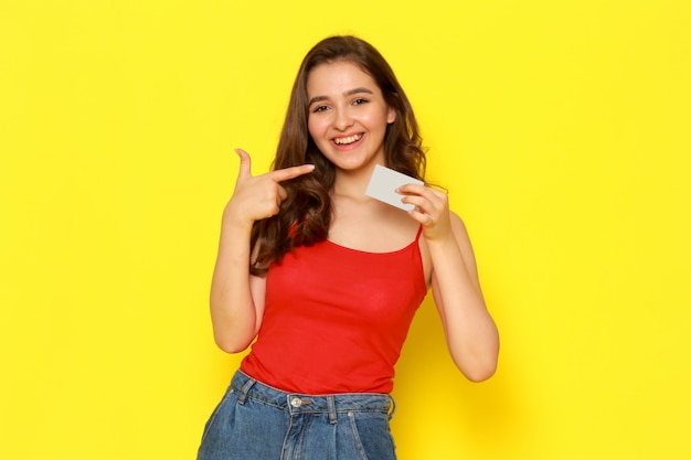 Een vooraanzicht jonge mooie dame in het rood shirt en spijkerbroek glimlachen