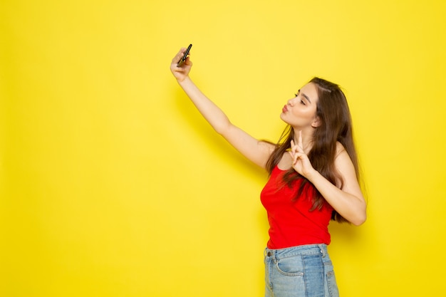 Een vooraanzicht jonge mooie dame in rood shirt en spijkerbroek nemen een selfie