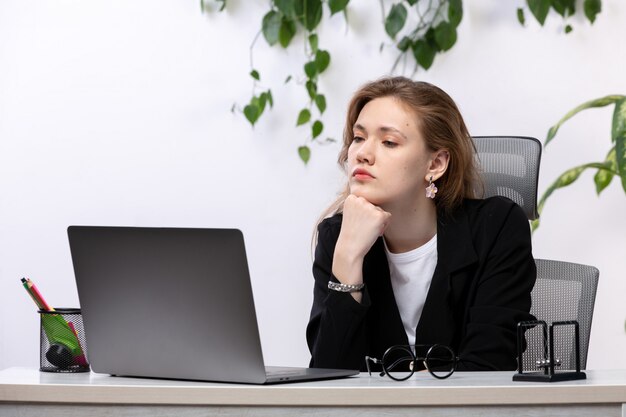 Een vooraanzicht jonge mooie dame in wit overhemd en zwarte jas met behulp van haar laptop voor tafel met bladeren hangen