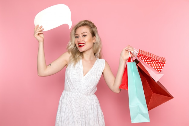 Een vooraanzicht jonge mooie dame in witte jurk bedrijf shopping pakketten met een glimlach op haar gezicht