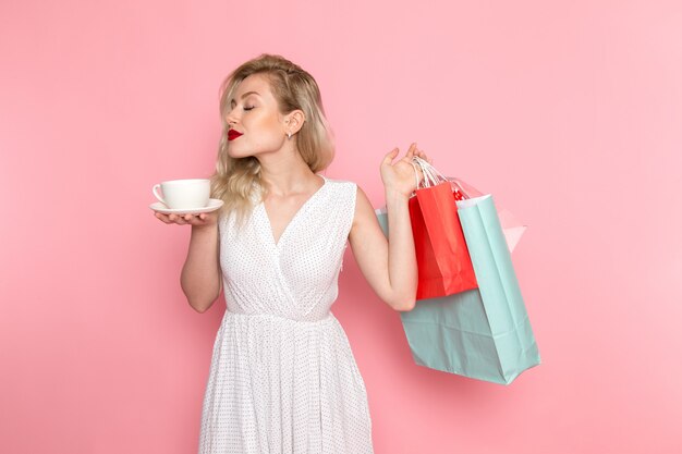 Een vooraanzicht jonge mooie dame in witte jurk met shopping pakketten en kopje thee