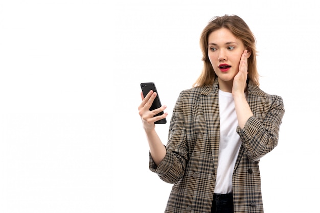 Een vooraanzicht jonge mooie dame in witte t-shirt zwarte jeans en jas met smartphone op de witte