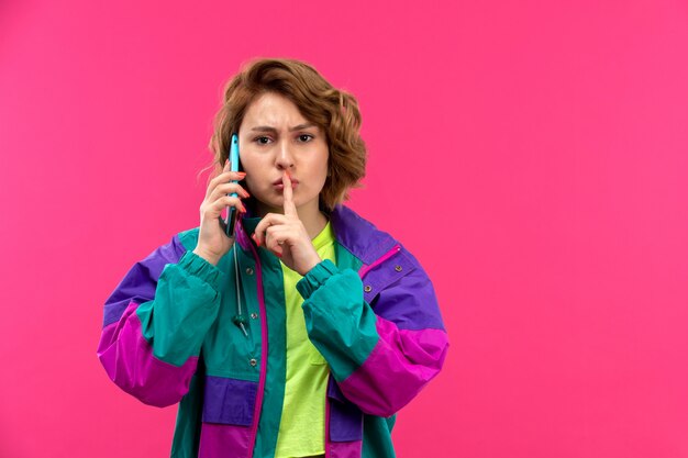 Een vooraanzicht jonge mooie dame in zuur gekleurde shirt zwarte broek kleurrijke jas praten aan de telefoon praten aan de telefoon