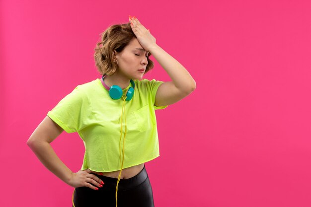 Een vooraanzicht jonge mooie dame in zuurkleurige shirt zwarte broek met blauwe koptelefoon teleurgesteld